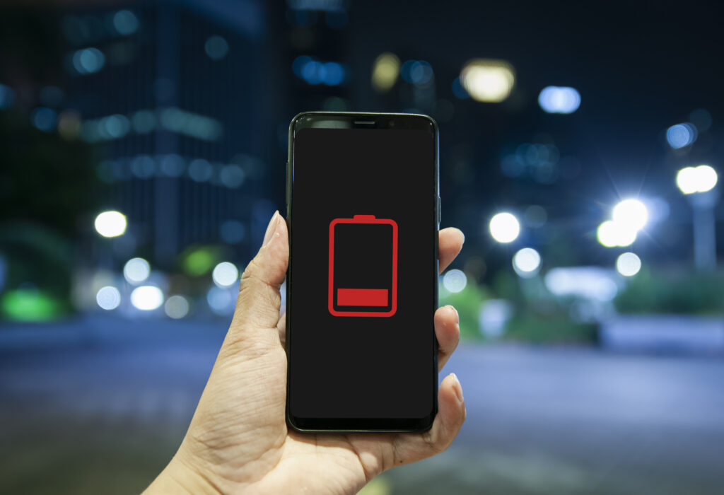 Close up of hand holding smart phone with low battery icon on screen. night bokeh background